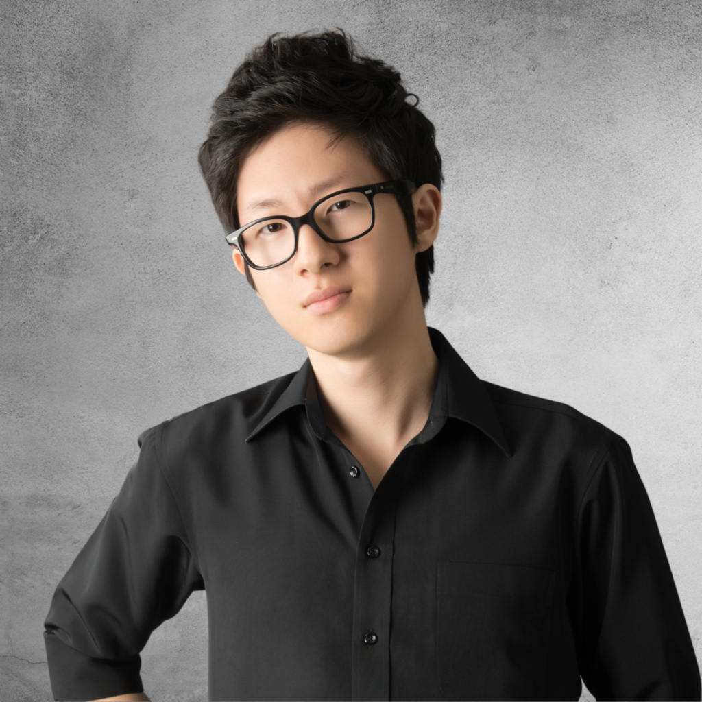 Close up shot of Kyoungsun Park in front of a grey background. He is wearing a black shirt and black glasses